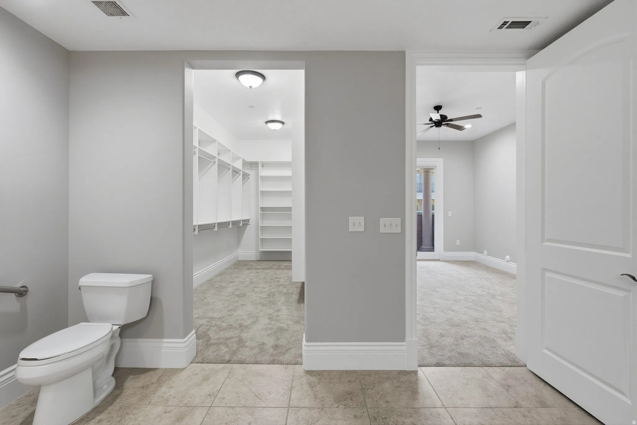 Tiled flooring, white baseboards, a walk-in closet with built-in shelving, and a ceiling fan with integrated lighting