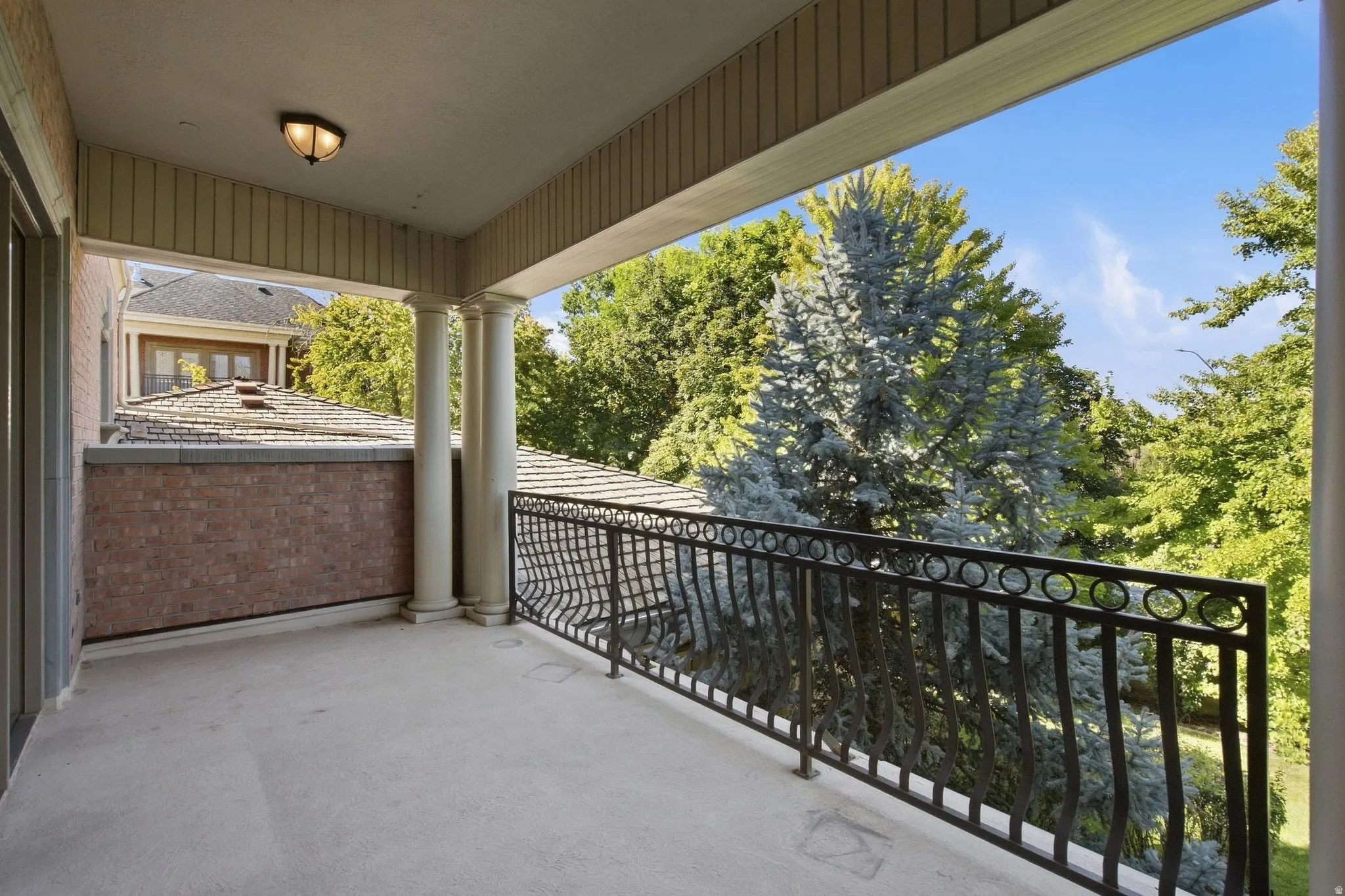 Covered balcony featuring concrete flooring, a decorative wrought iron railing, and fluted columns