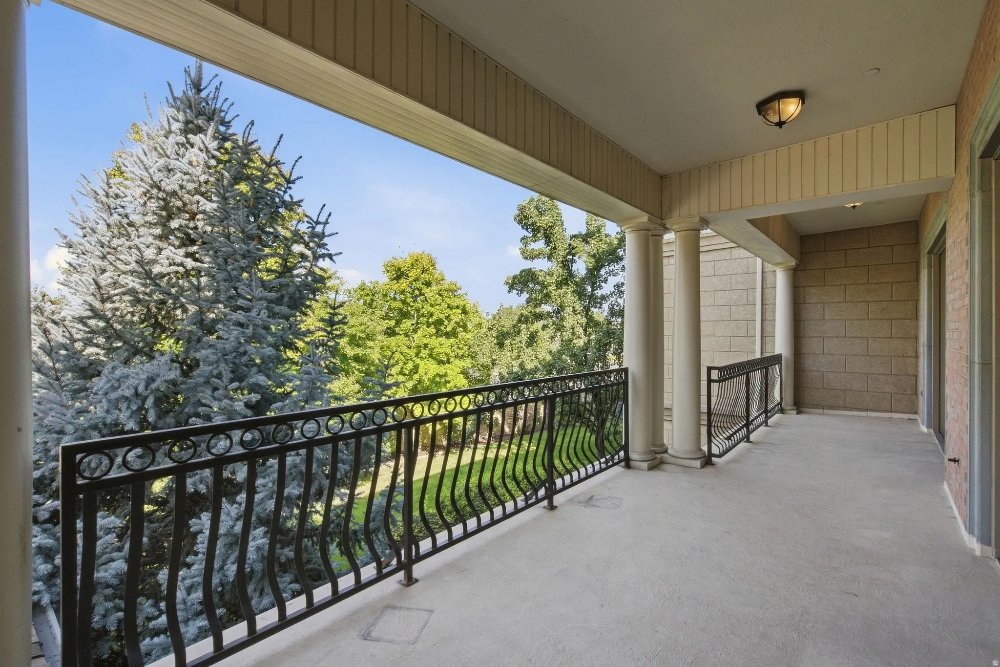 Spacious balcony featuring concrete flooring, black wrought iron railings, and multiple support columns