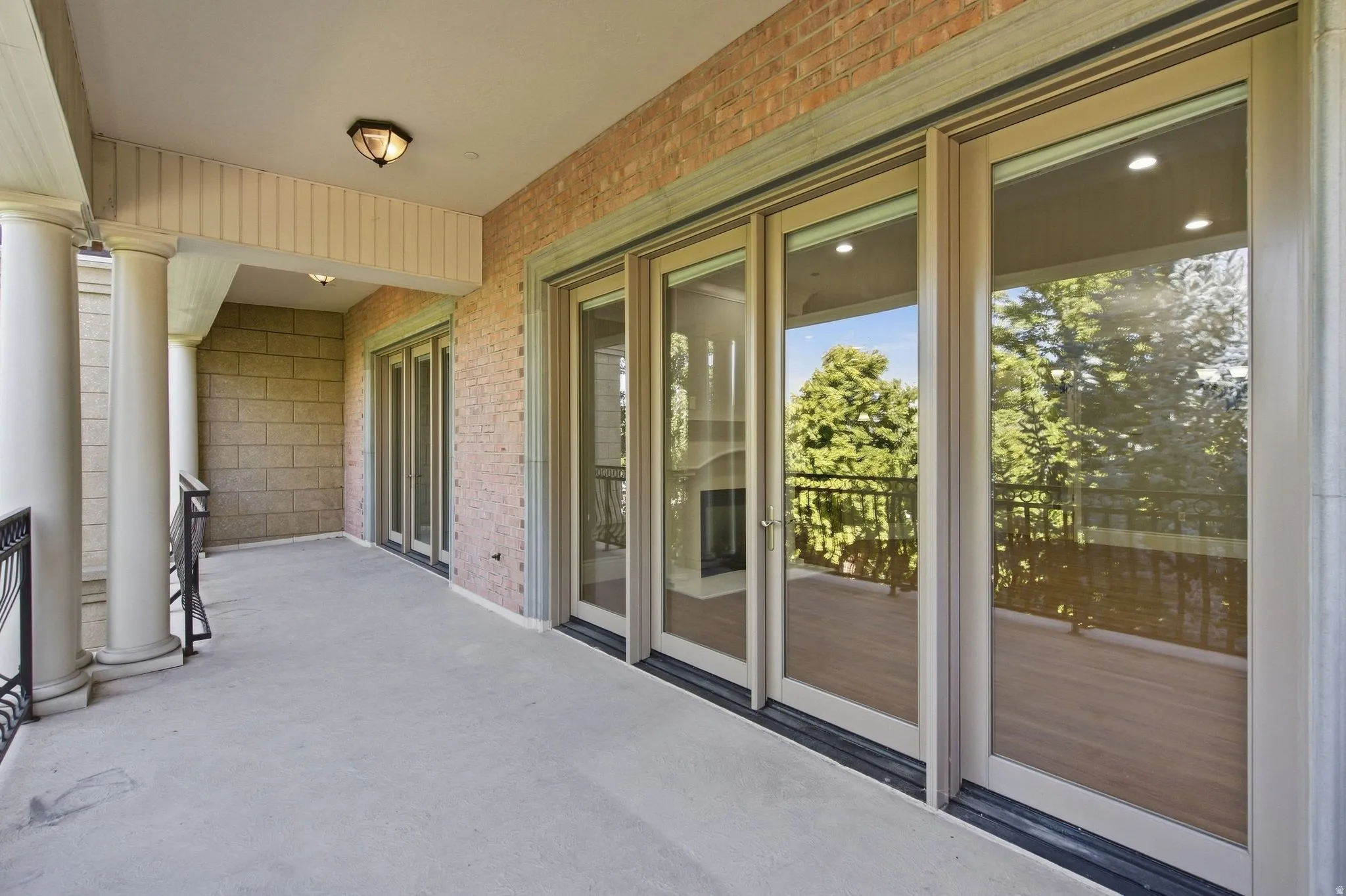 Private balcony featuring a concrete surface, brick exterior, decorative columns, and multiple glass panel doors