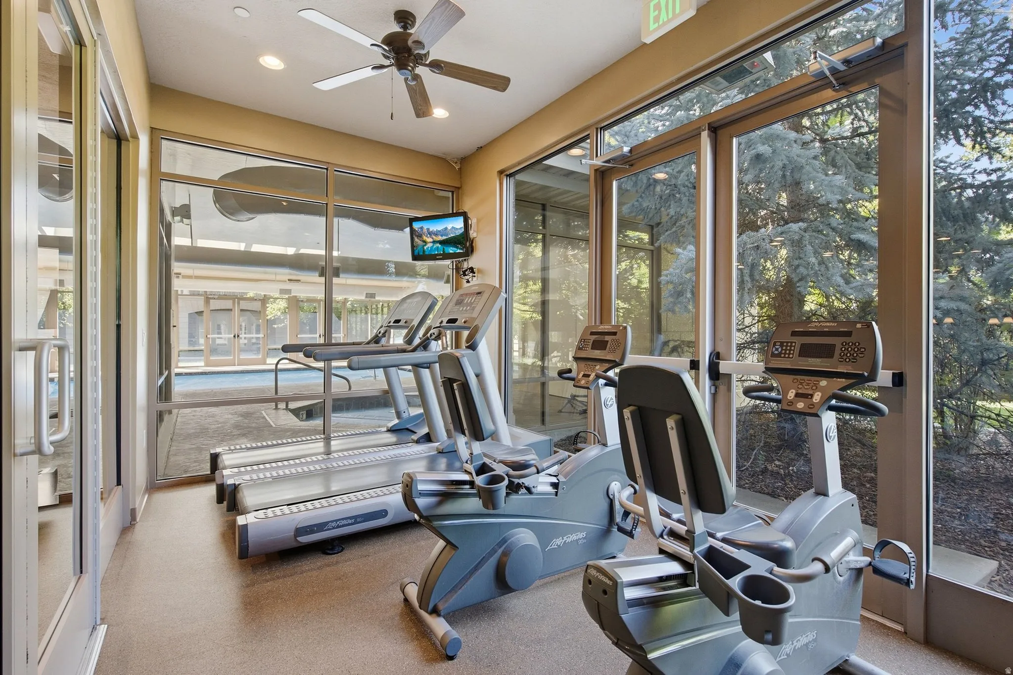 Fitness area with exercise equipment, ceiling fan, recessed lighting, wall-mounted television, and floor-to-ceiling windows