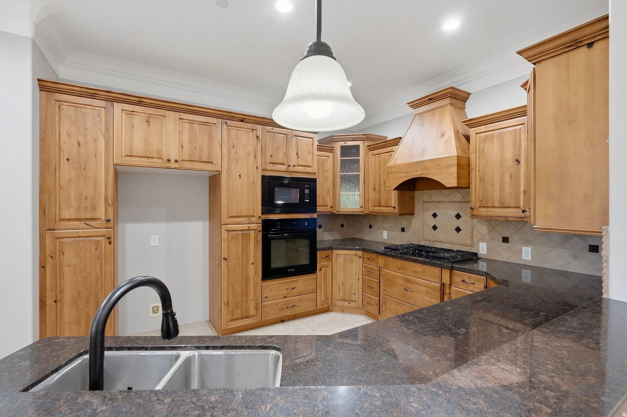 Extensive wood cabinetry, dark stone countertops, integrated microwave and oven, gas cooktop, and a double basin stainless steel sink