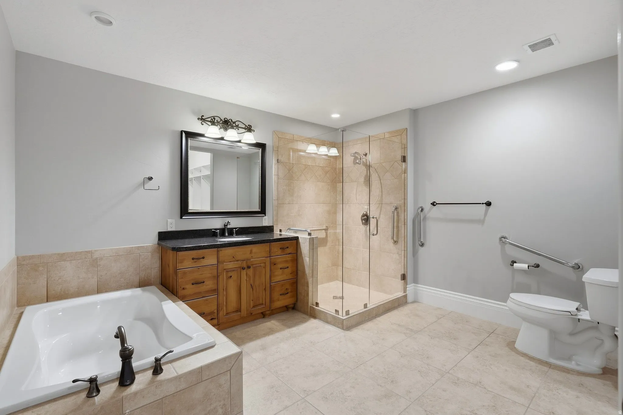 Tiled soaking tub, wood vanity with dark countertop, glass-enclosed shower, tiled flooring, and recessed lighting