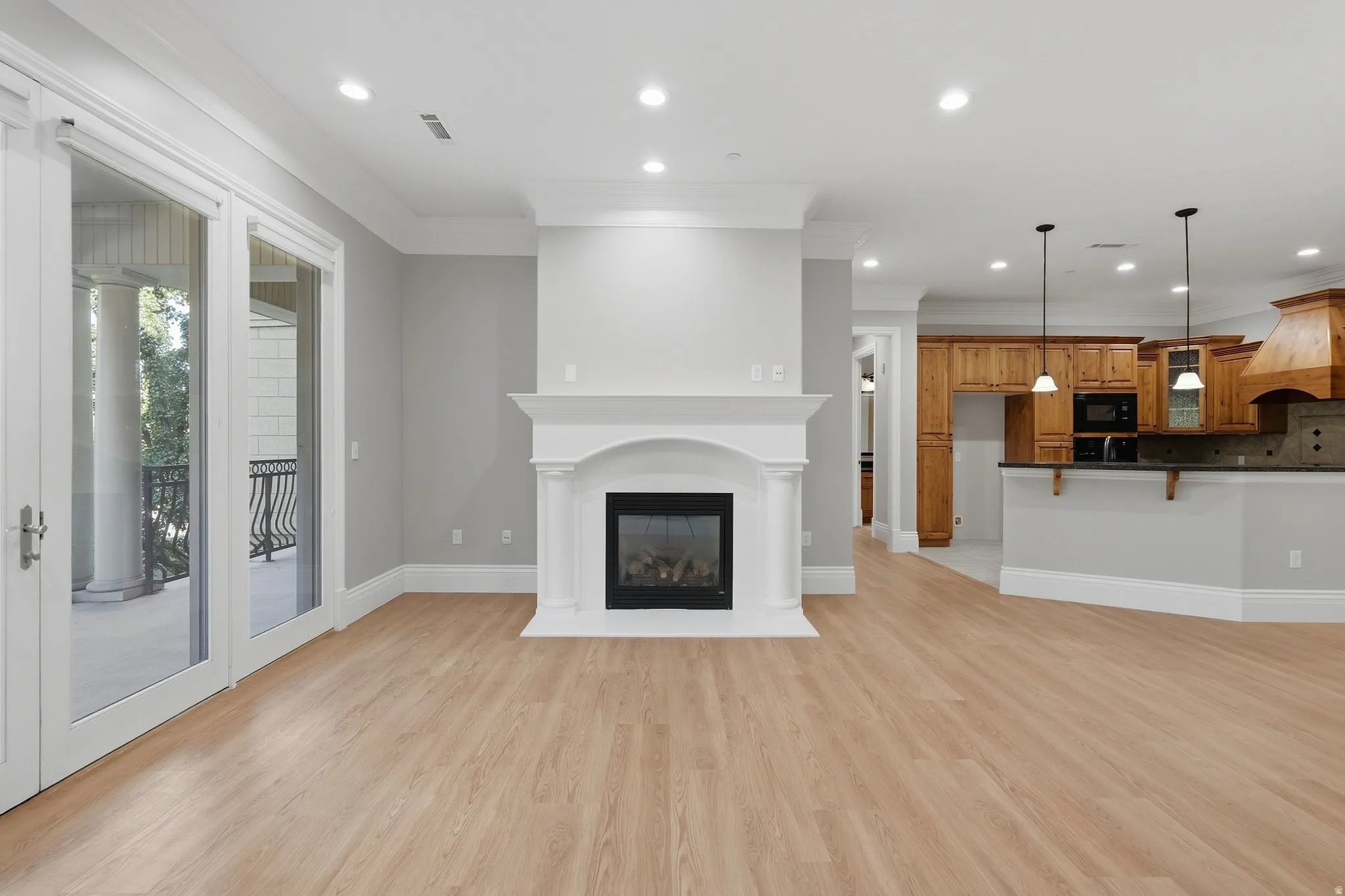 Wood-finish flooring throughout, white fireplace with mantle, recessed lighting, double glass doors to balcony, and a kitchen with wood cabinetry
