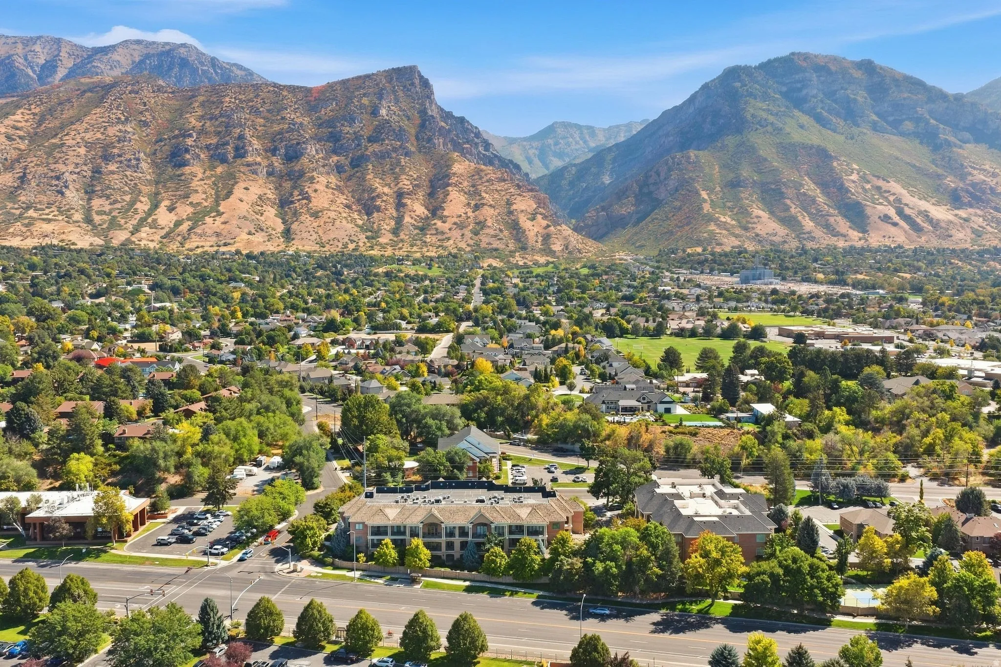 Expansive residential area with abundant mature trees, surrounded by towering mountain ranges