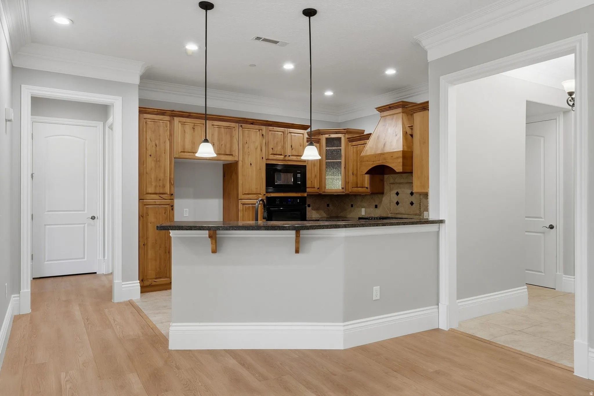 Kitchen featuring natural wood cabinetry, dark countertops, black appliances, and pendant lighting