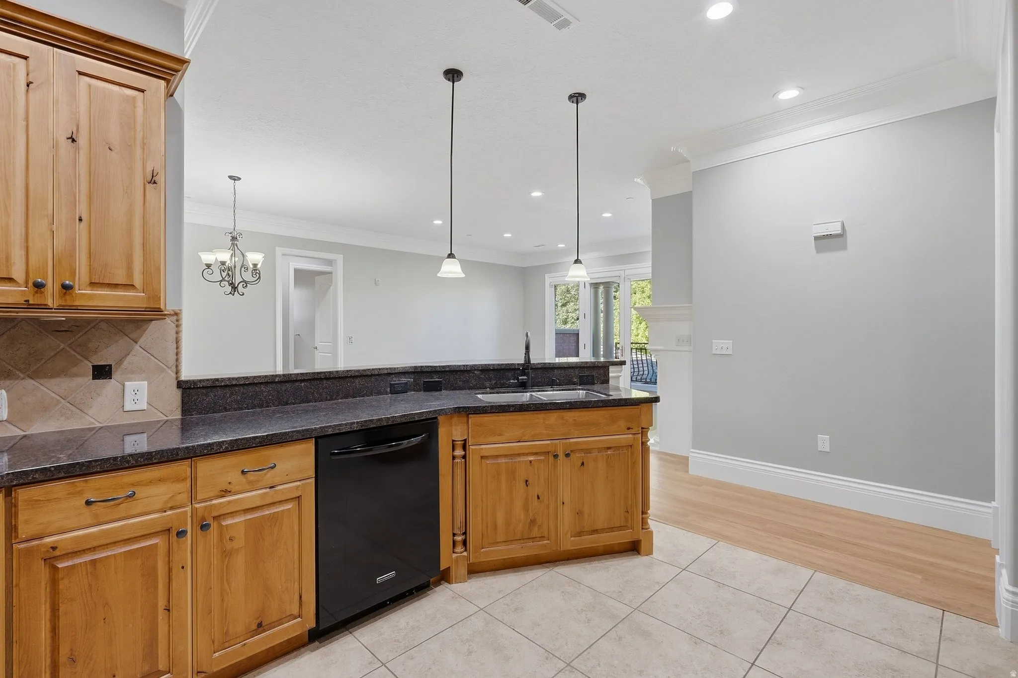 Wood cabinetry with dark hardware, dark countertops, built-in dishwasher, tile flooring, and pendant lighting