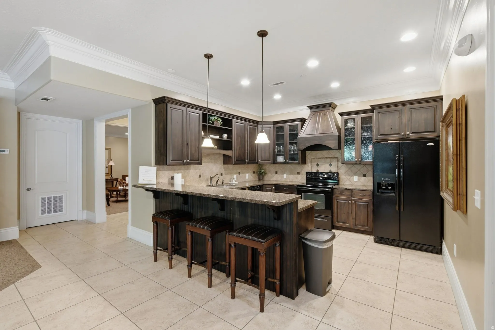 Kitchen with dark wood cabinetry, a breakfast bar with pendant lighting, tile flooring, and matching tile backsplash