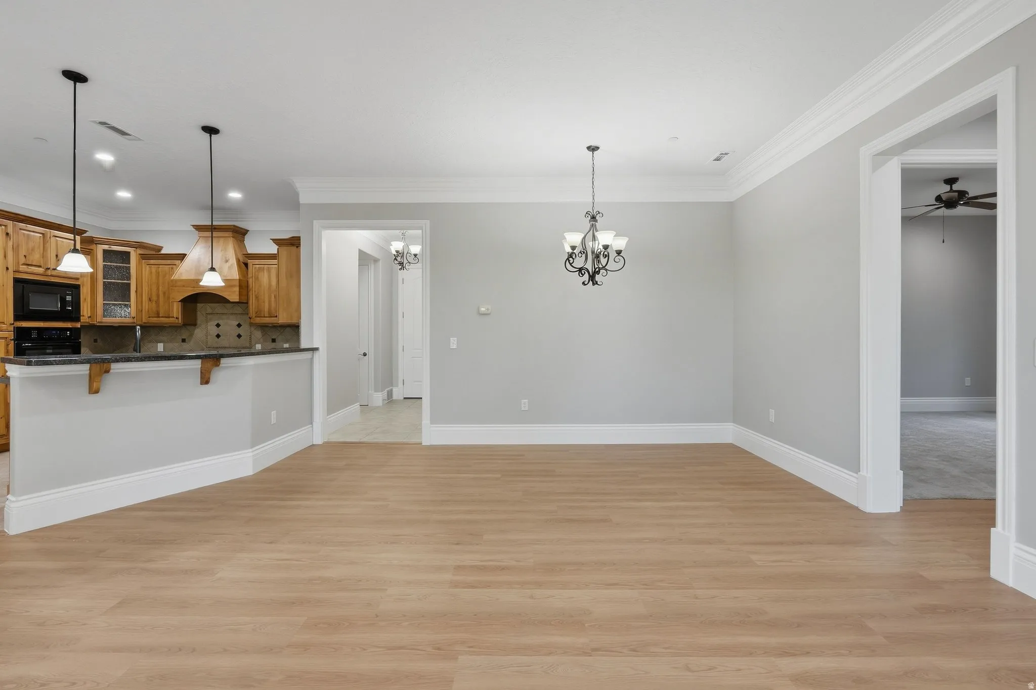Wood-finish flooring, crown molding, a kitchen with wood cabinetry, a built-in microwave, and pendant lighting, and an overhead chandelier