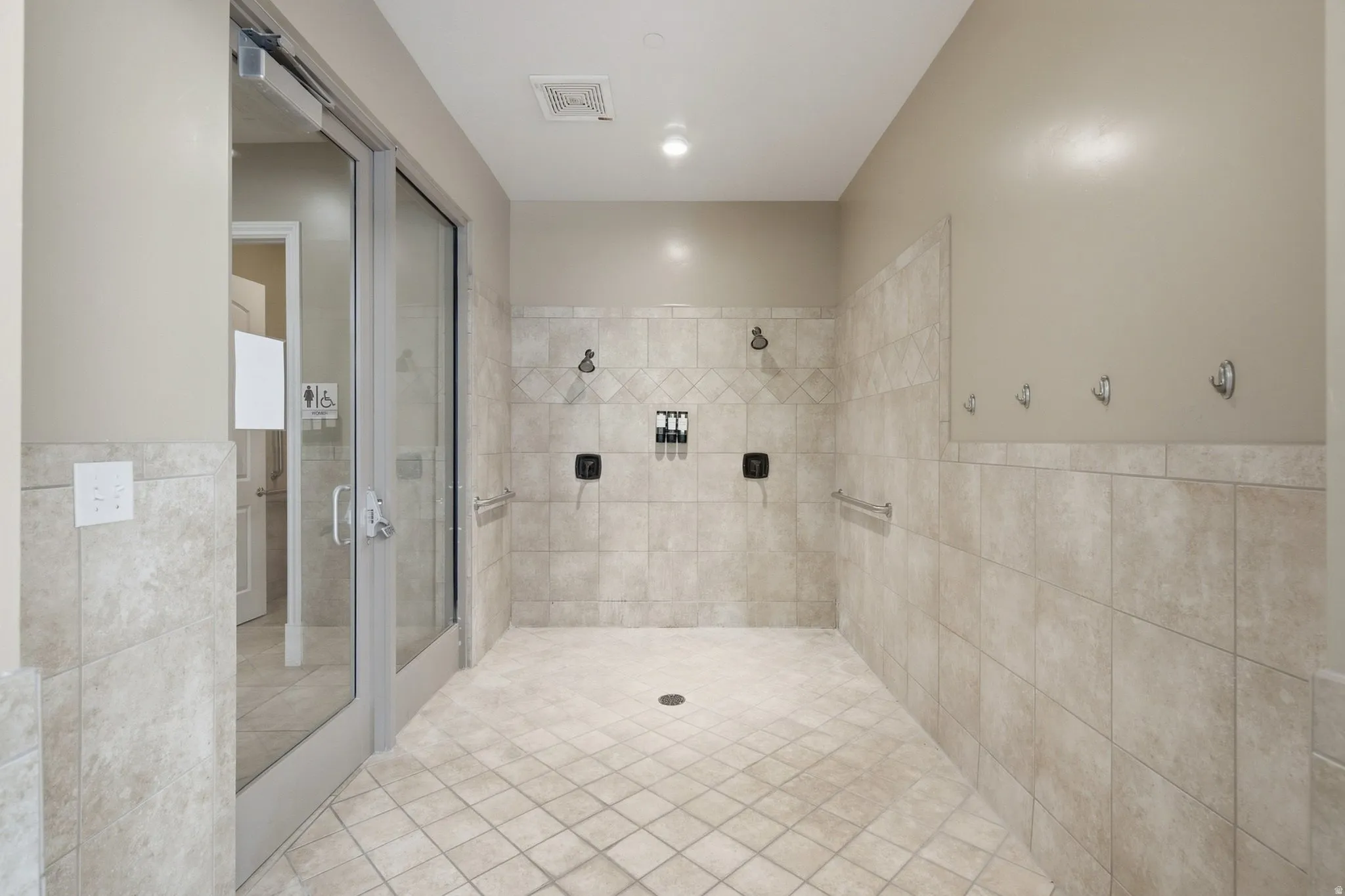 Tile flooring with a diamond pattern, multiple shower heads, wall-mounted grab bars, and a glass-paneled door