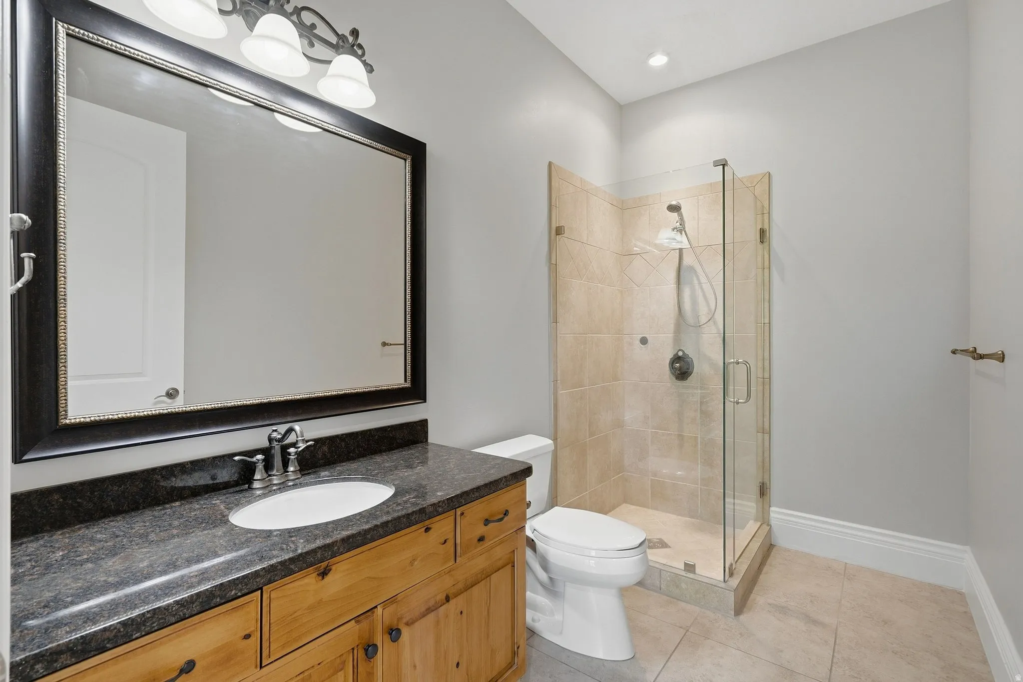 Glass-enclosed shower with tile surround, wood-finish vanity with dark countertop, and large framed mirror