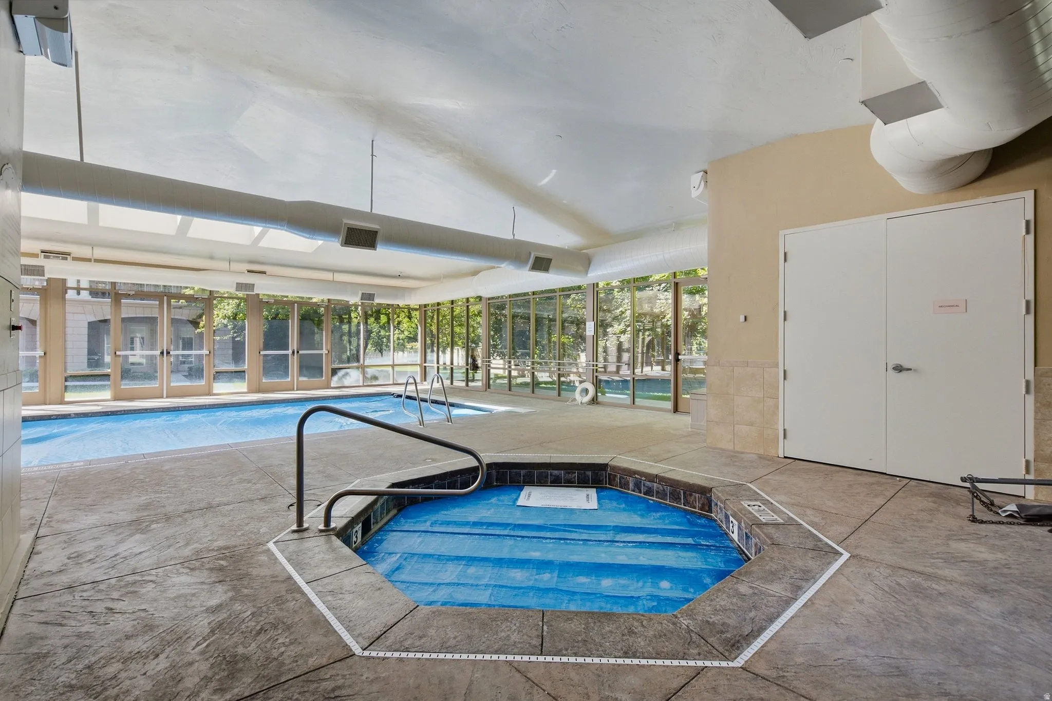 Indoor swimming pool with an integrated spa, expansive glass panel walls, and stamped concrete flooring