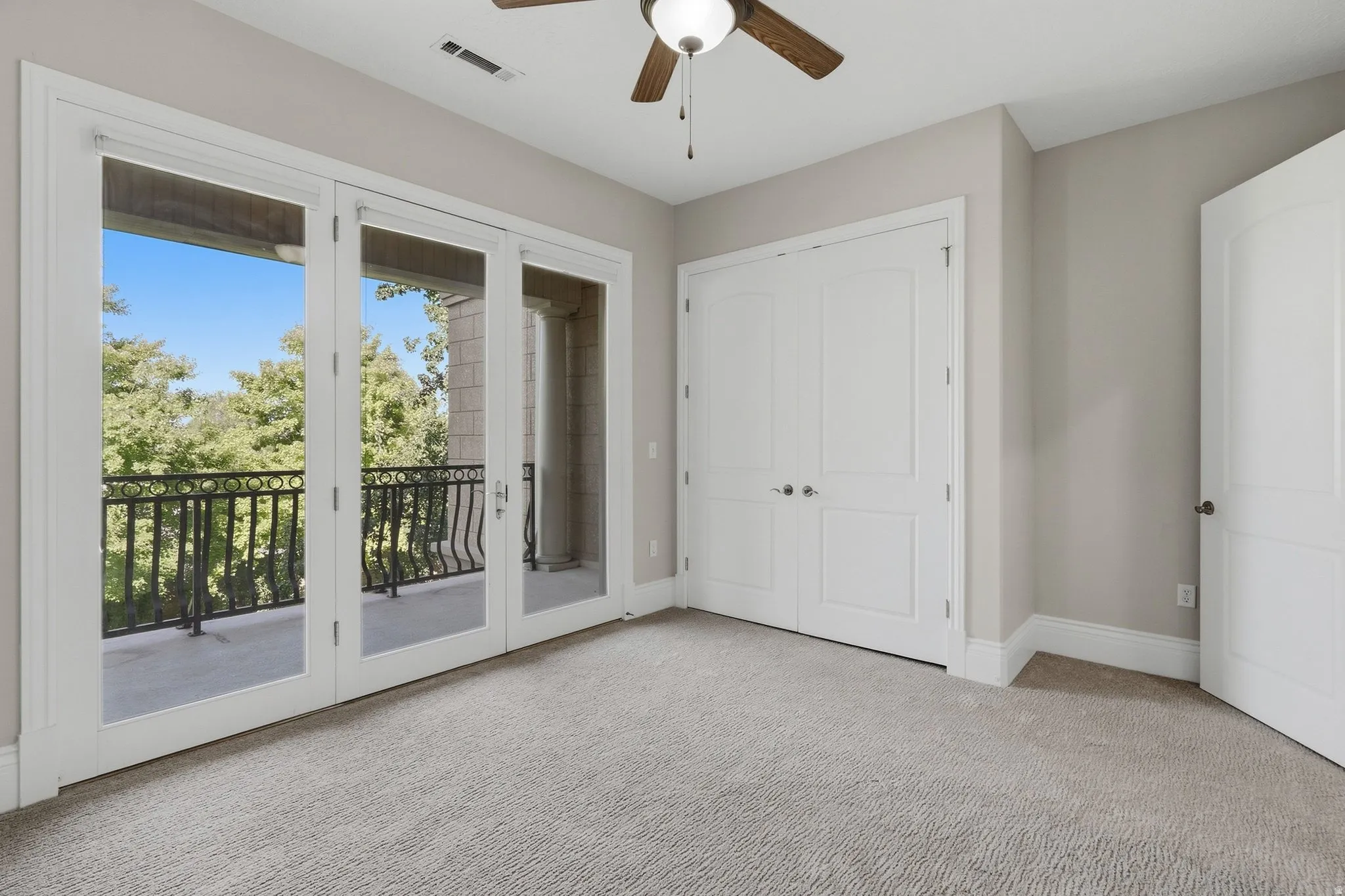 Patio doors with a wrought iron railing, neutral wall color, built-in closet, ceiling fan with light fixture, and carpeted flooring