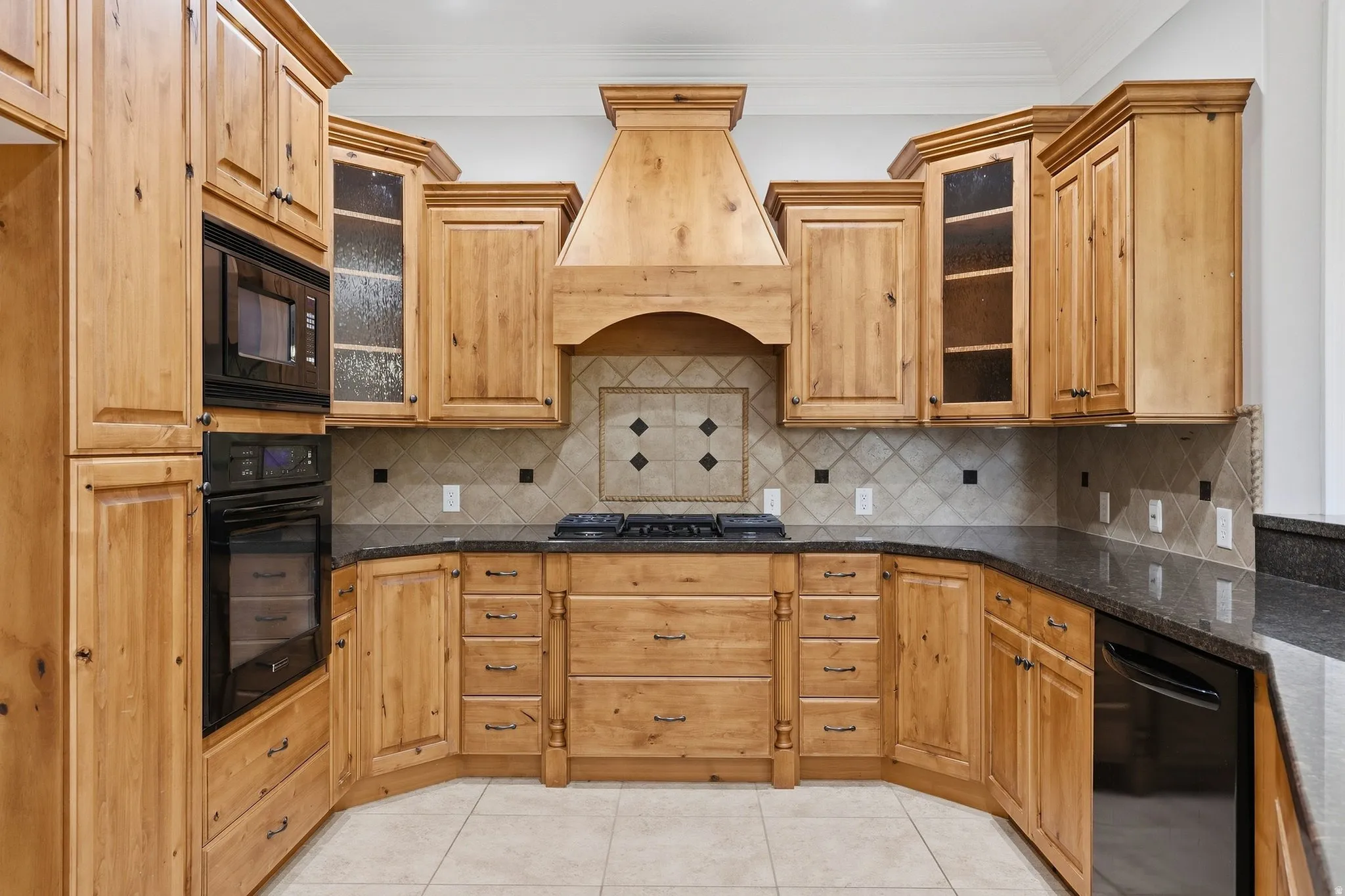 U-shaped kitchen with wood cabinetry, black countertops, built-in microwave and oven, and a tiled backsplash with decorative accents