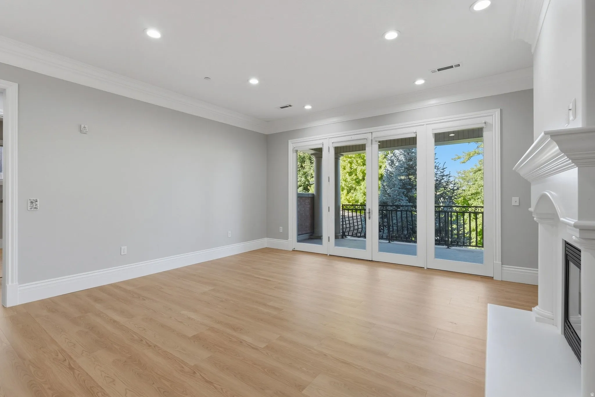 Expansive room featuring wood-finish flooring, recessed lighting, crown molding, a built-in fireplace, and French doors opening to a balcony with black railings