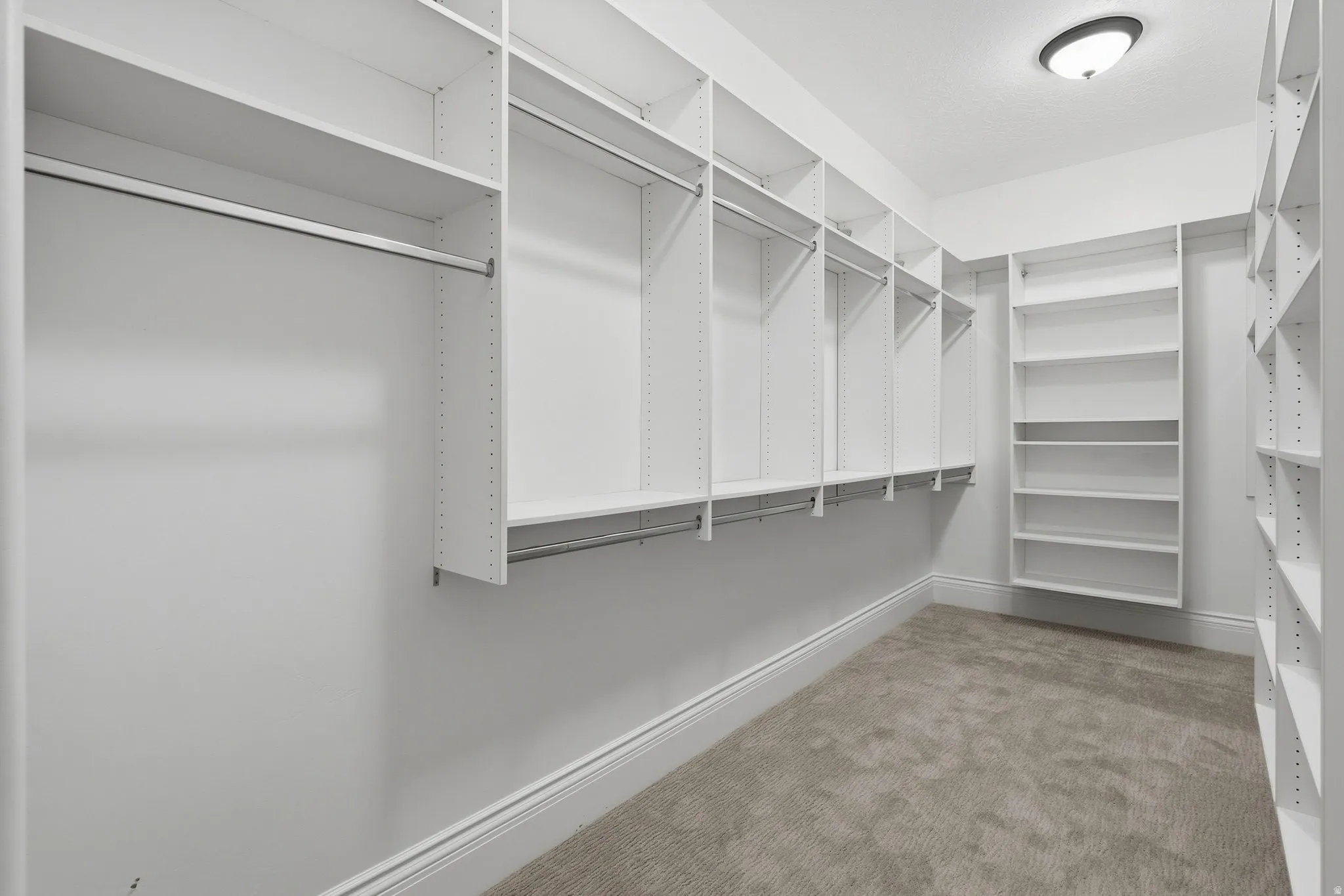 Wall-to-wall custom closet organization system featuring multiple hanging rods, adjustable shelving, and recessed ceiling light fixture
