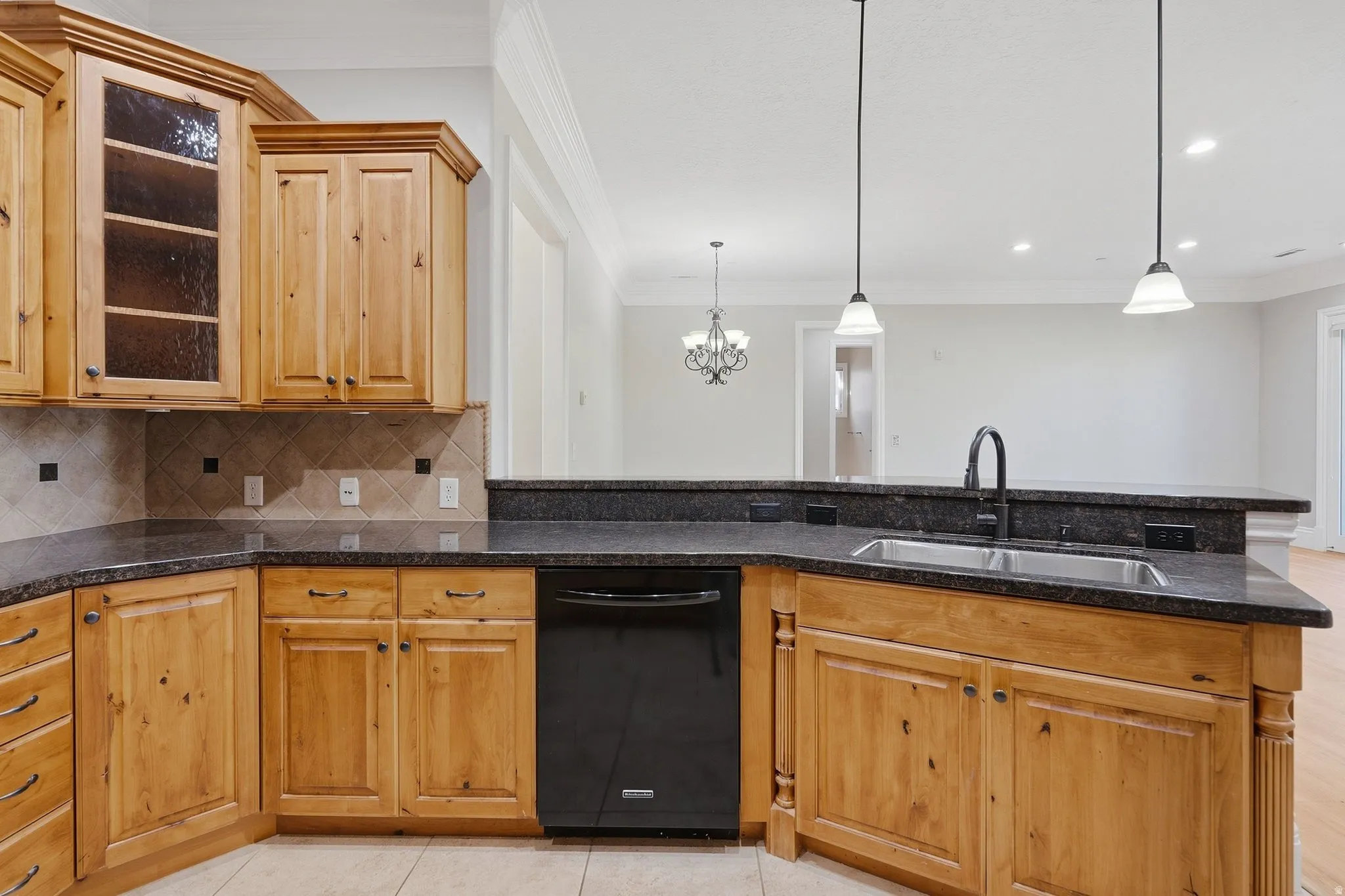 Kitchen featuring wood cabinetry, dark countertops, a stainless steel sink with a gooseneck faucet, a black built-in dishwasher, and pendant lighting