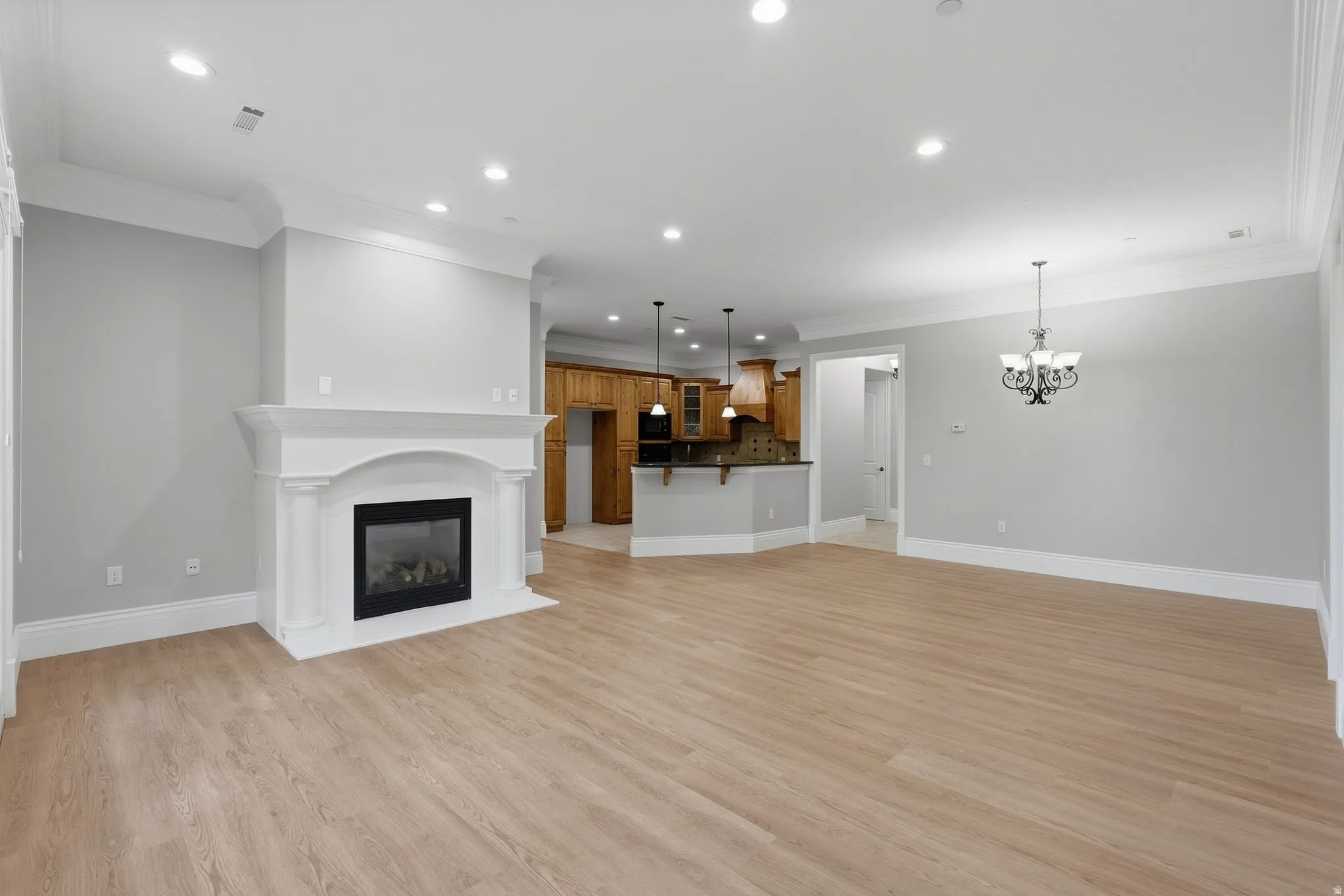 Open-concept living space with wood-finish flooring, recessed lighting, a white mantel fireplace, and crown molding