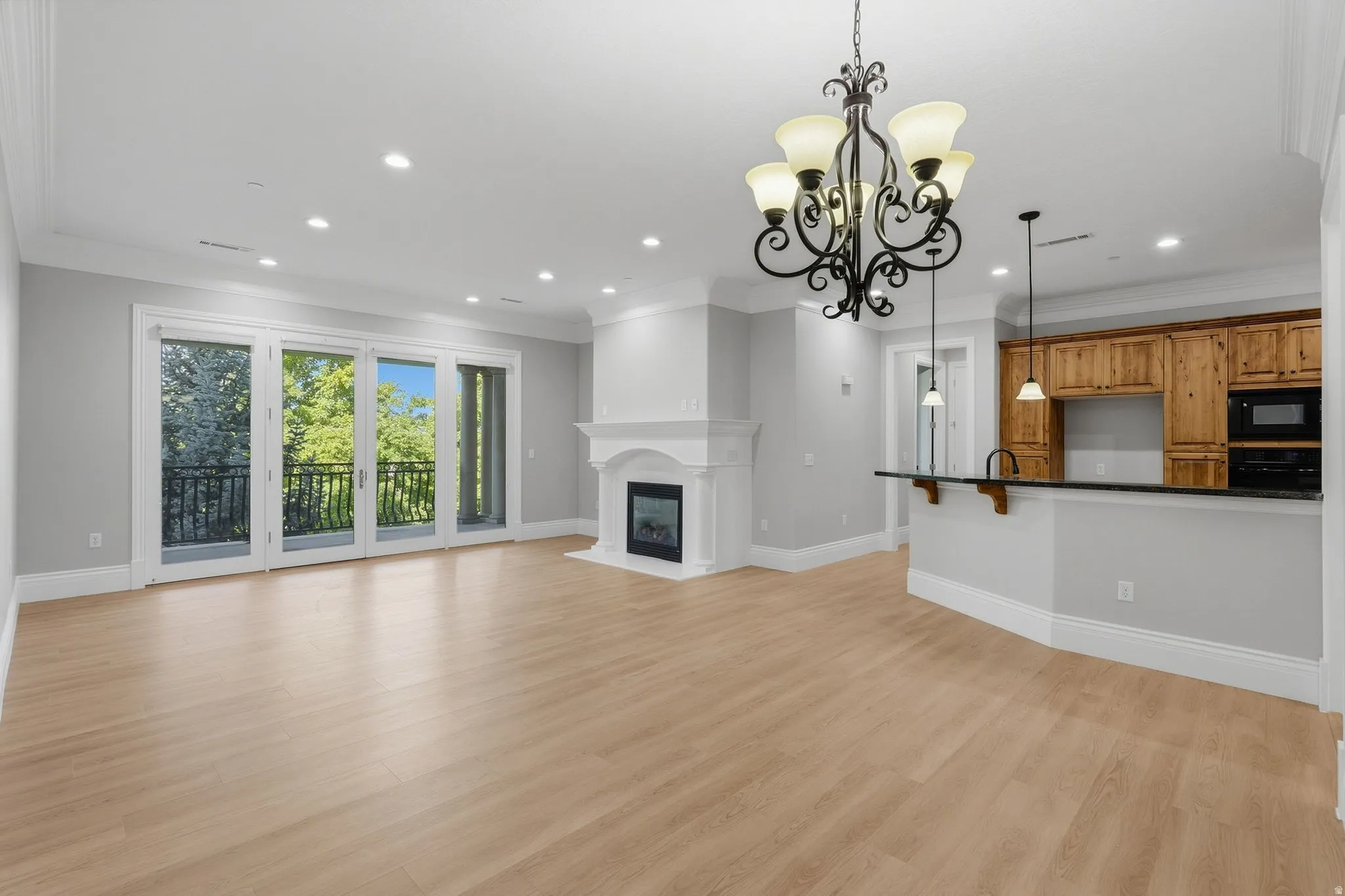 Light wood-finish flooring with a white fireplace mantel, recessed lighting, and crown molding