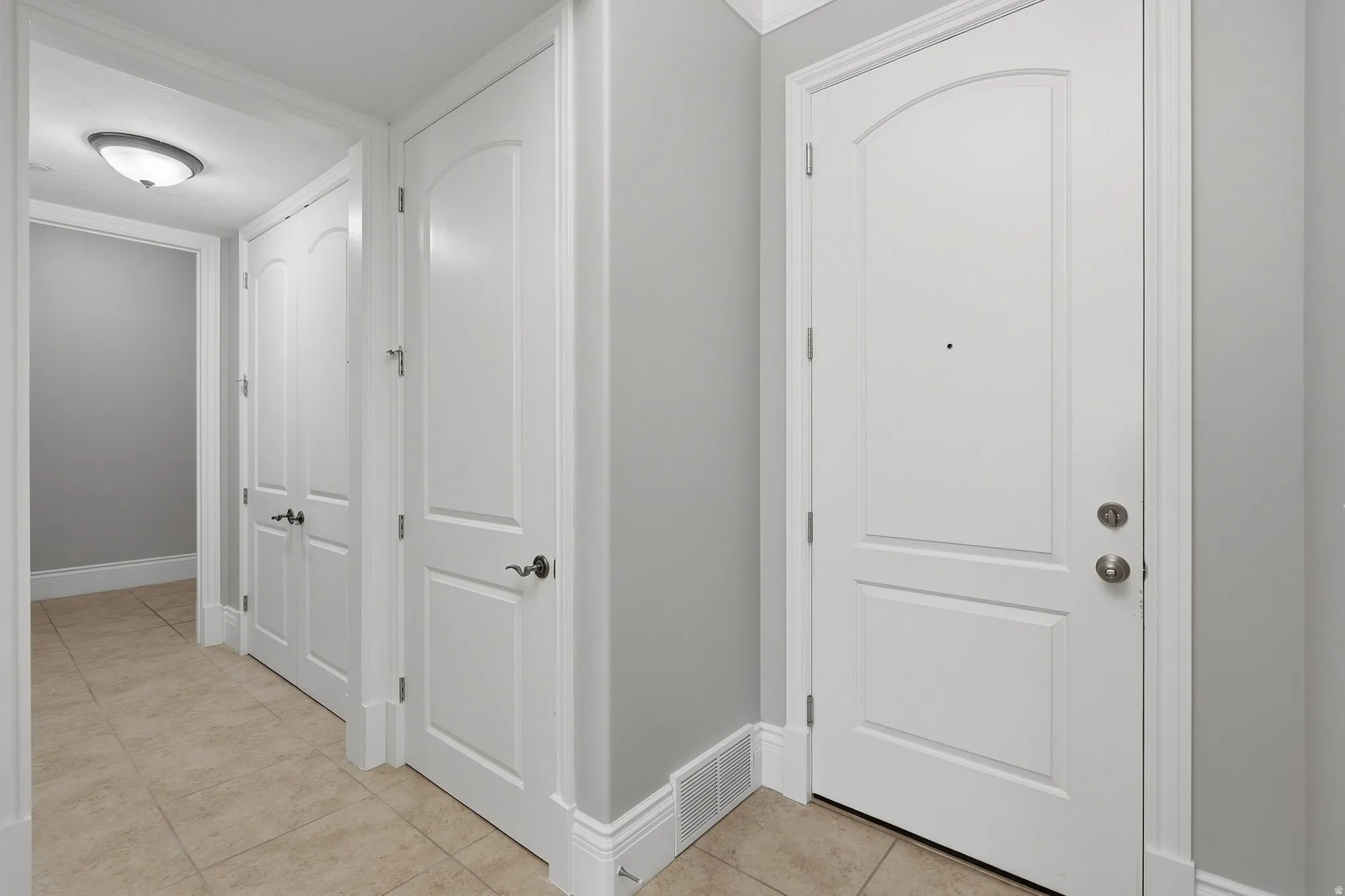 Arched panel entry door, three panel interior doors, flush mount ceiling light fixture, tile flooring, and light gray wall paint