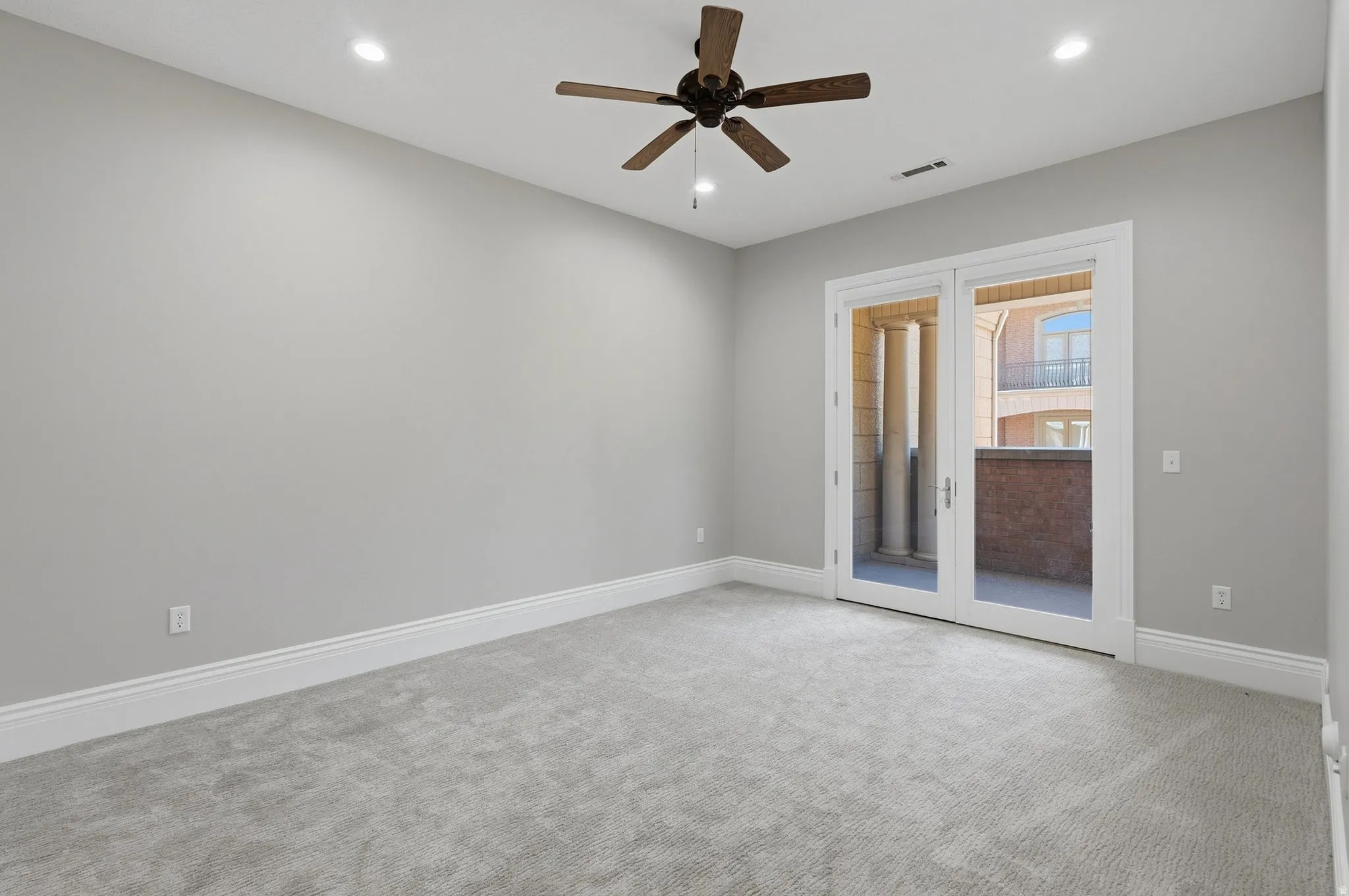 Plush carpet flooring, recessed lighting, ceiling fan, and French doors opening to a private balcony with architectural columns