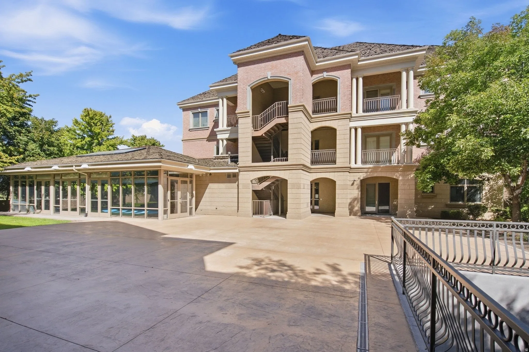 Multi-story building featuring stucco and brick exterior, multiple balconies with balustrades, an exterior staircase, and an enclosed pool area with large windows
