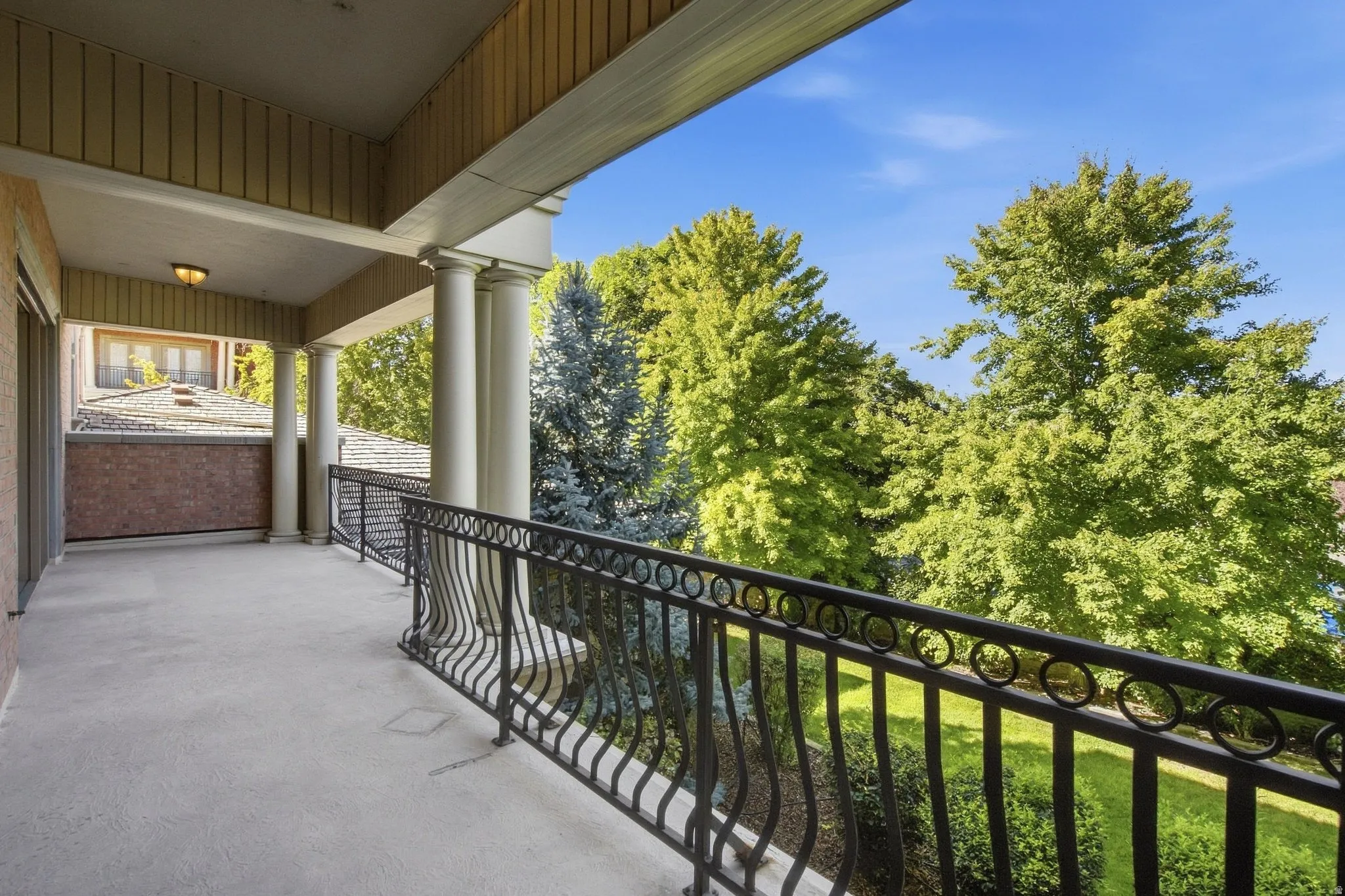 Covered outdoor balcony with a concrete floor, decorative black metal railing, and architectural columns