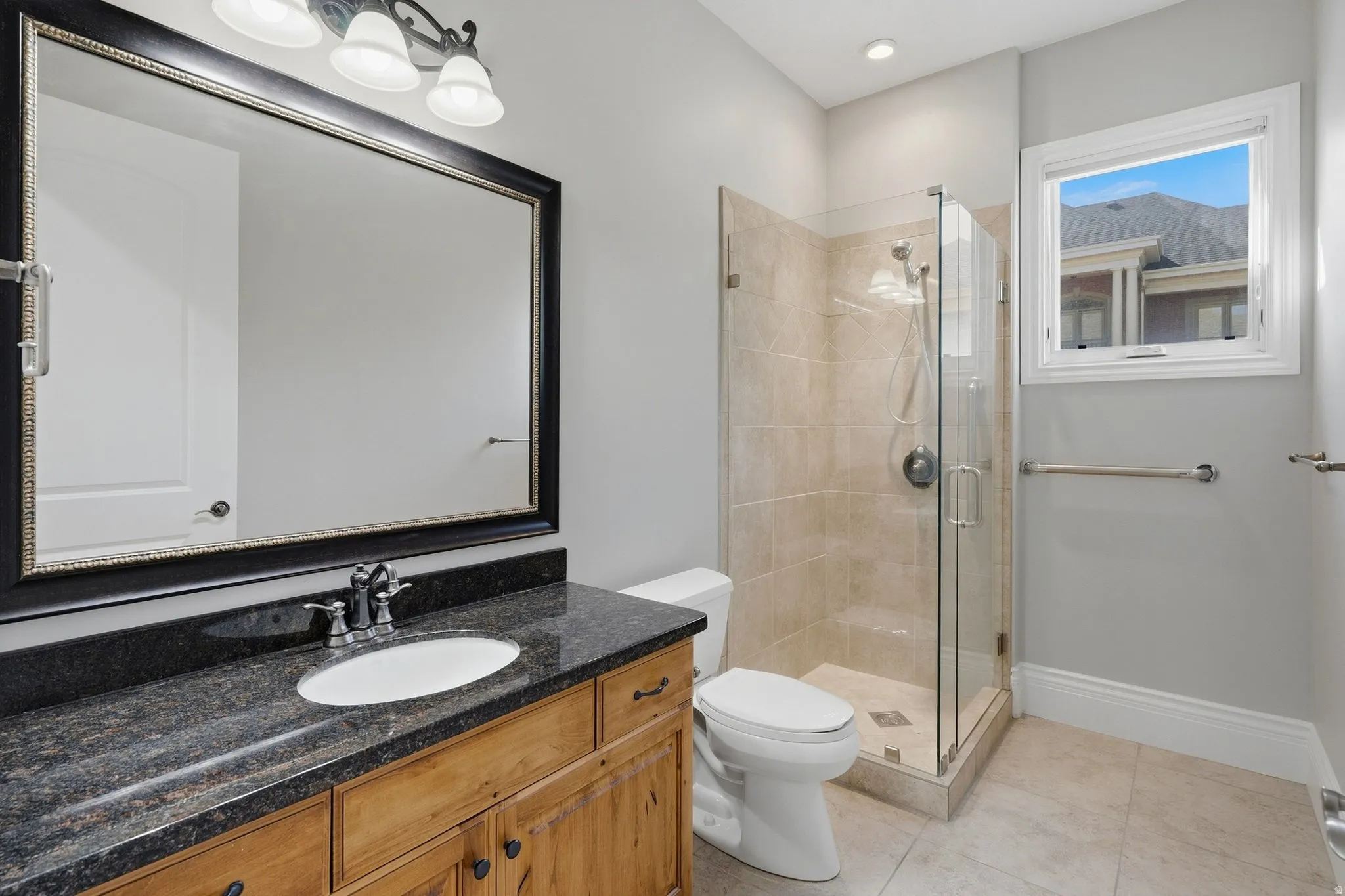 Wood-finish vanity with dark speckled countertop, undermount sink, and framed mirror