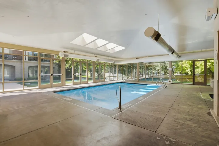 Indoor swimming pool featuring skylights, extensive glass paneling, and concrete surround