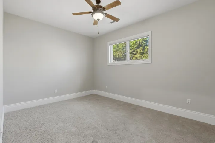Neutral-toned walls, light-hued carpeting, white window trim, and a ceiling fan with integrated lighting