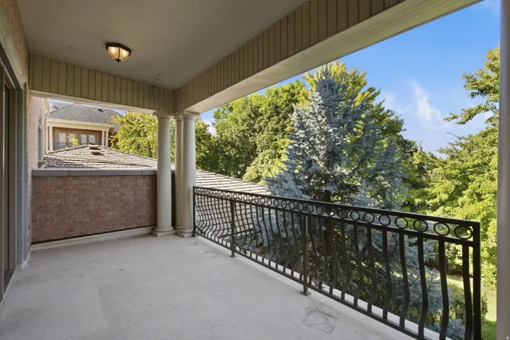 Covered balcony featuring concrete flooring, a decorative wrought iron railing, and fluted columns