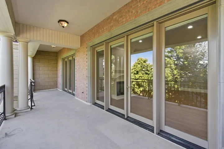 Private balcony featuring a concrete surface, brick exterior, decorative columns, and multiple glass panel doors