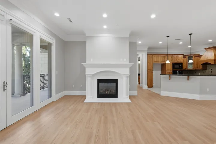 Wood-finish flooring throughout, white fireplace with mantle, recessed lighting, double glass doors to balcony, and a kitchen with wood cabinetry