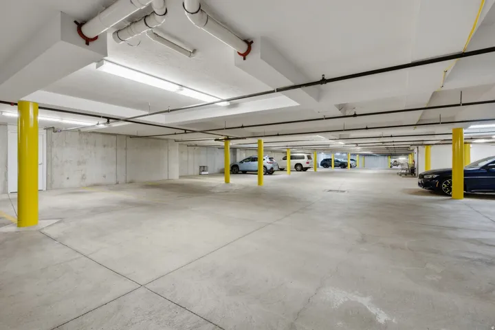 Underground parking garage with concrete flooring, exposed ceiling piping, and fluorescent lighting
