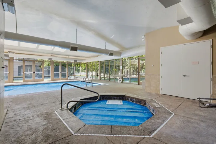 Indoor swimming pool with an integrated spa, expansive glass panel walls, and stamped concrete flooring