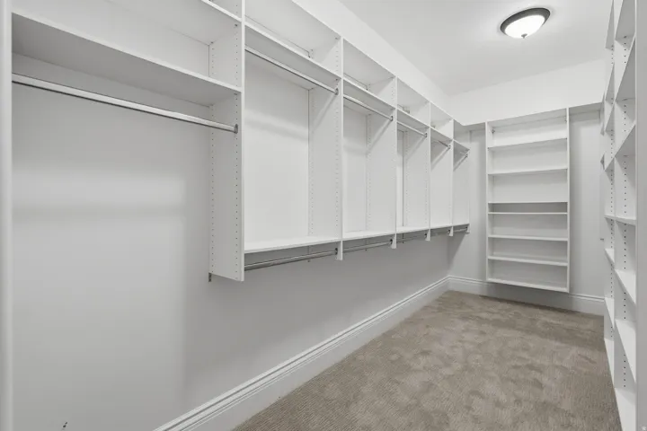 Wall-to-wall custom closet organization system featuring multiple hanging rods, adjustable shelving, and recessed ceiling light fixture