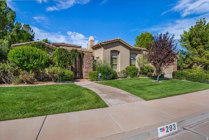 Stucco exterior with stone accents, mature landscaping, tiled roof, curved concrete pathway, and an ornamental entry gate