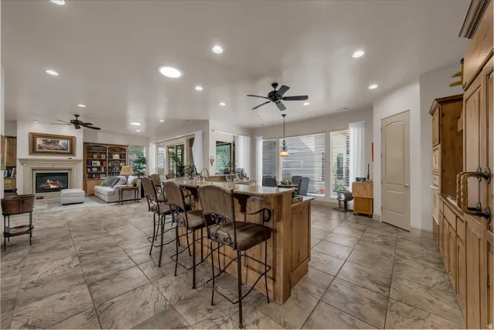 Stone tile flooring, central kitchen island with built-in cabinetry, recessed lighting, ceiling fans, and a fireplace with stone surround
