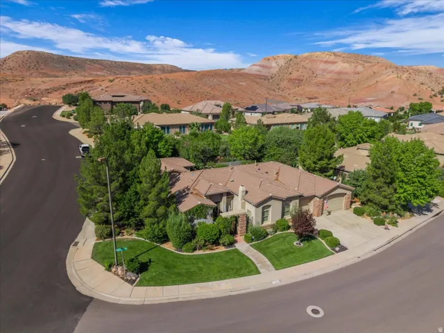 Corner lot residence featuring a paved driveway, mature landscaping, and a tile roof