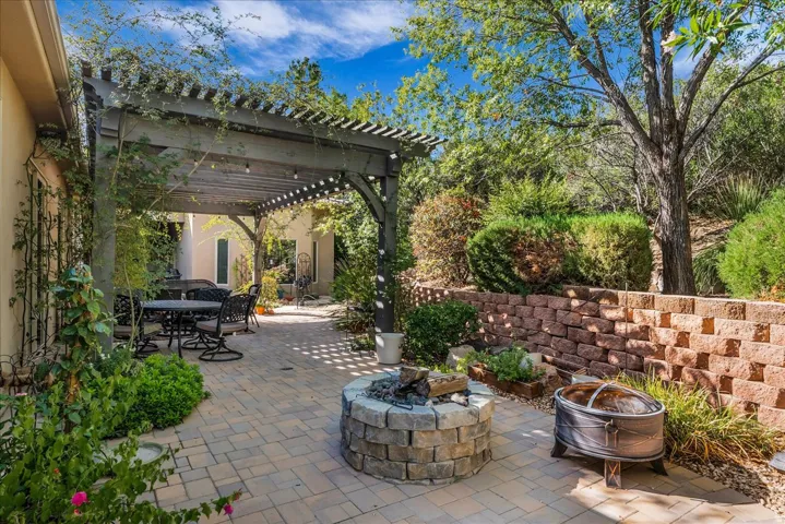 Expansive paver patio featuring a wood pergola, built-in stone fire pit, and tiered retaining wall