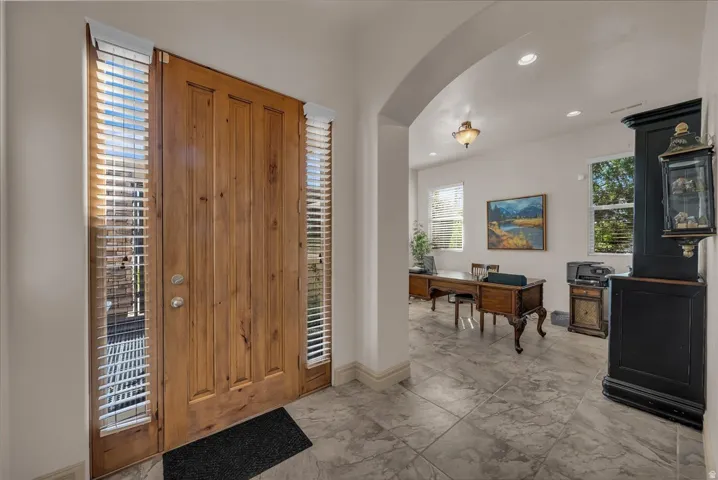 Wood-paneled front door with sidelights, arched doorway, recessed lighting, and tile flooring