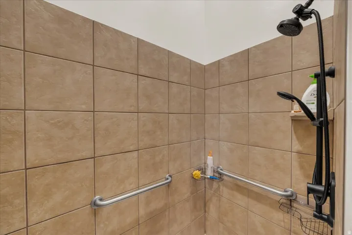 Tiled shower stall featuring two grab bars, a built-in niche, and a matte black shower system with a handheld spray
