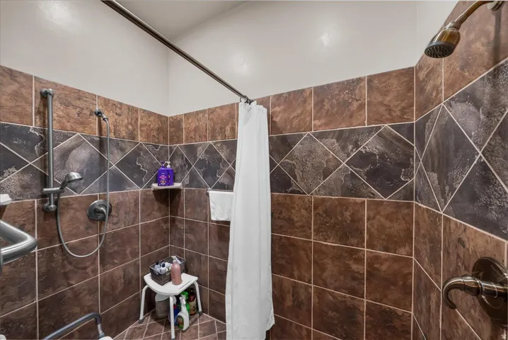 Tiled shower enclosure featuring a decorative accent band, handheld shower fixture, and wall-mounted grab bars