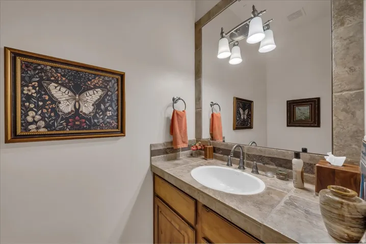 Warm wood cabinetry, stone-finish countertop, undermount sink with a dark-finish faucet, and a large wall-mounted mirror
