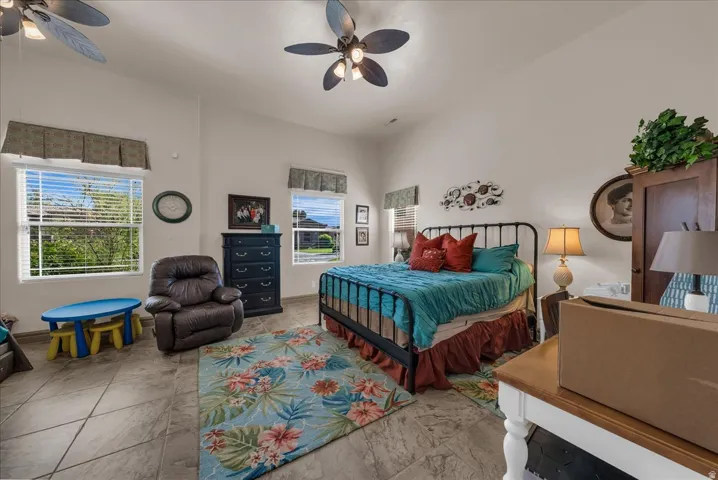 Vaulted ceilings with ceiling fans, multiple windows, tiled flooring, and a decorative bed frame