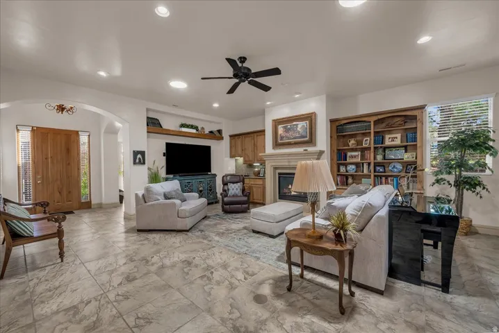 Arched entryway, tile flooring, built-in shelving, stone fireplace, and a ceiling fan