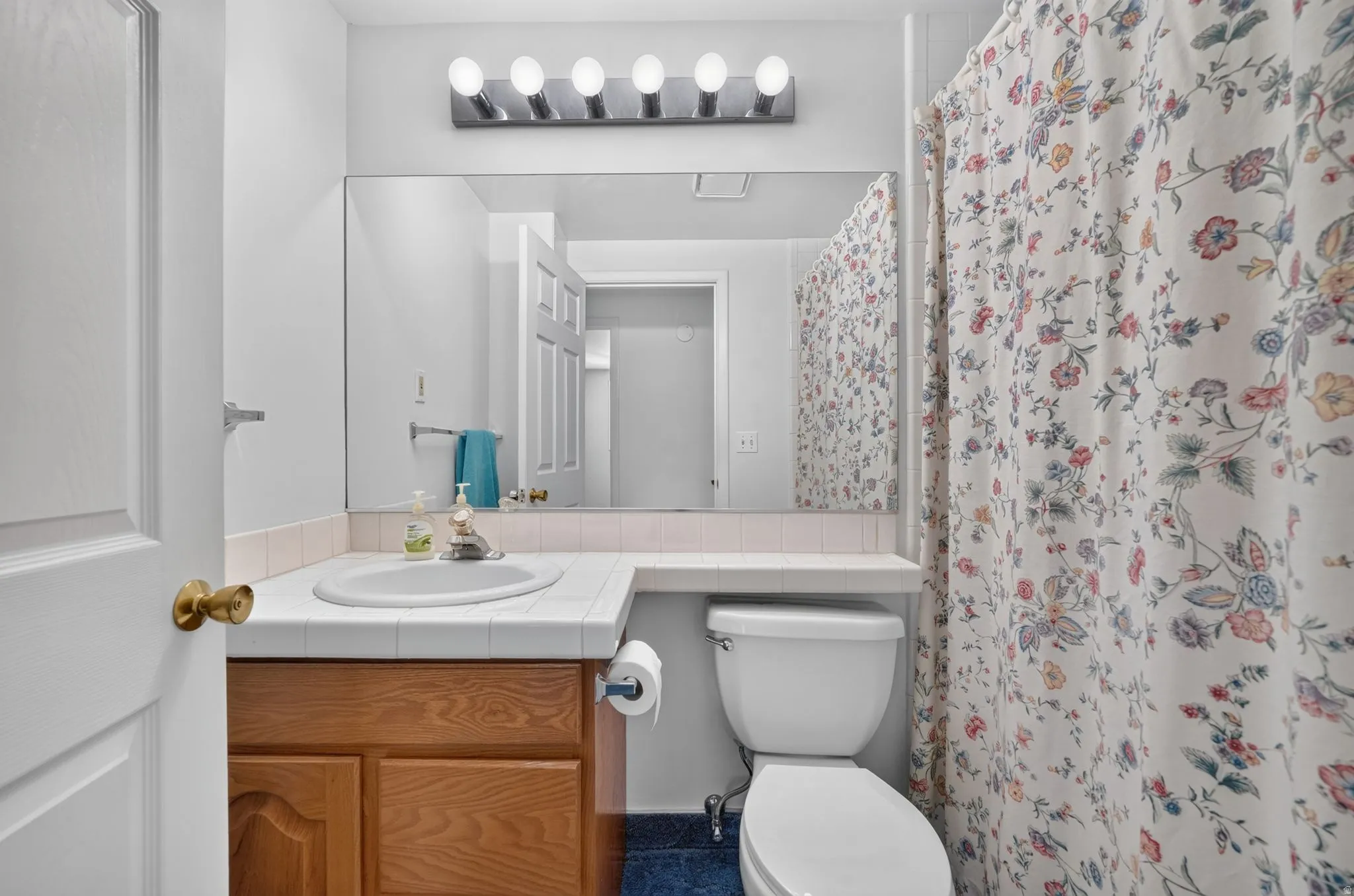 Vanity with natural wood-finish cabinetry, tile countertop with an integrated sink, and an expansive wall-mounted mirror