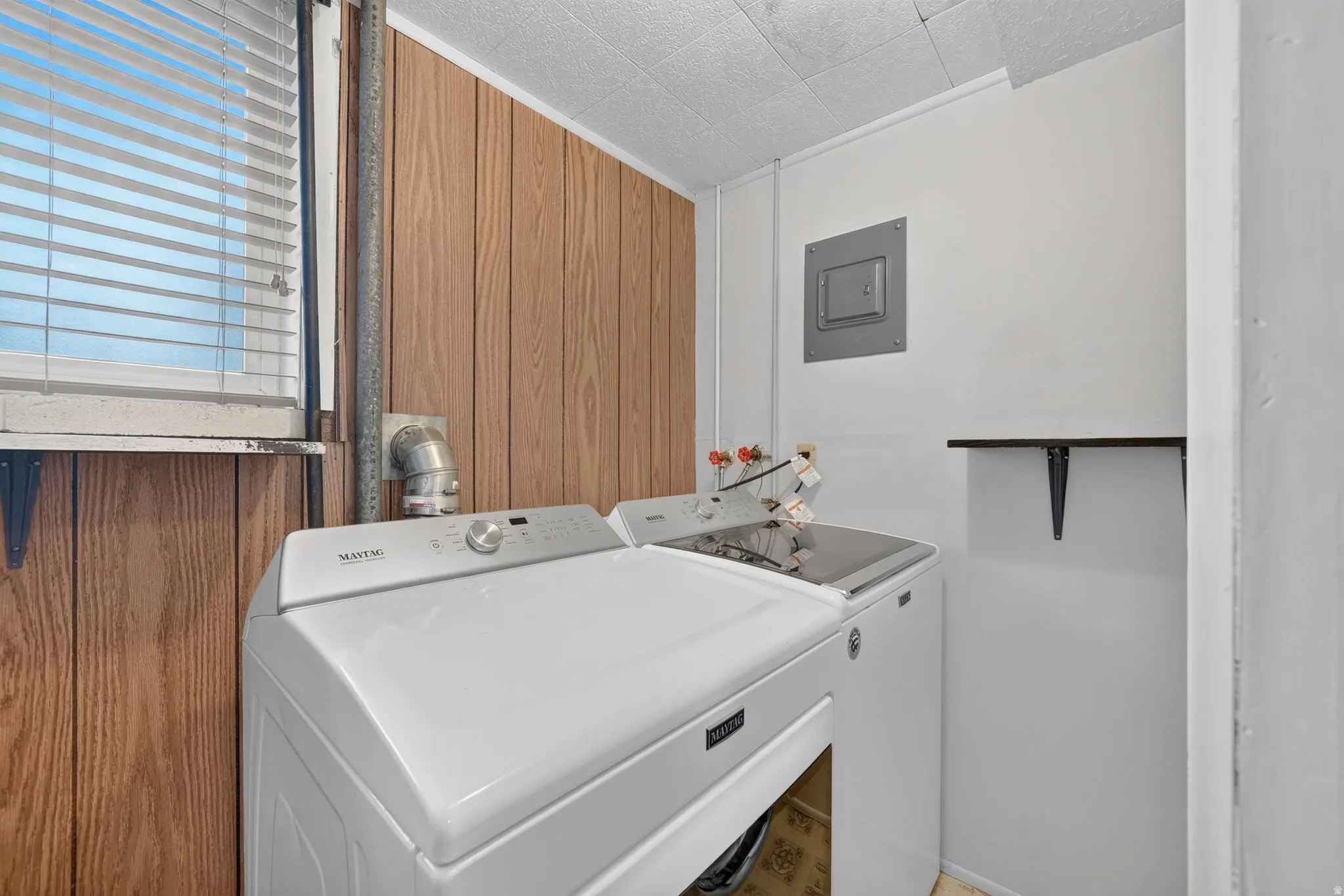 Utility room with wood-panel accent wall and a window with blinds