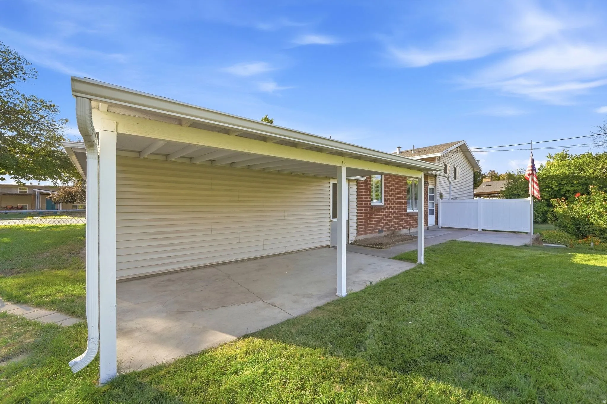 Covered patio area with concrete surfacing, adjacent to a manicured lawn and a white privacy fence