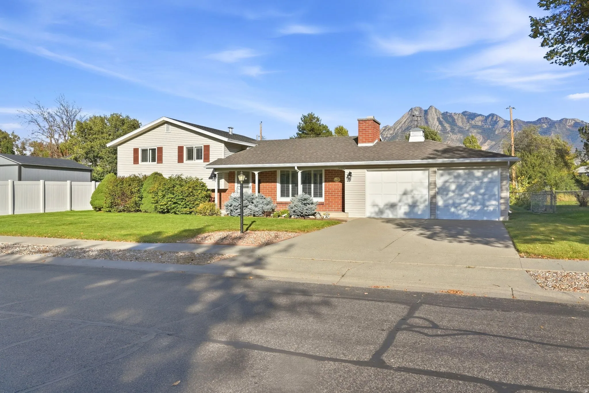 Exterior featuring a brick facade, attached two-car garage, established front landscaping, and a paved driveway